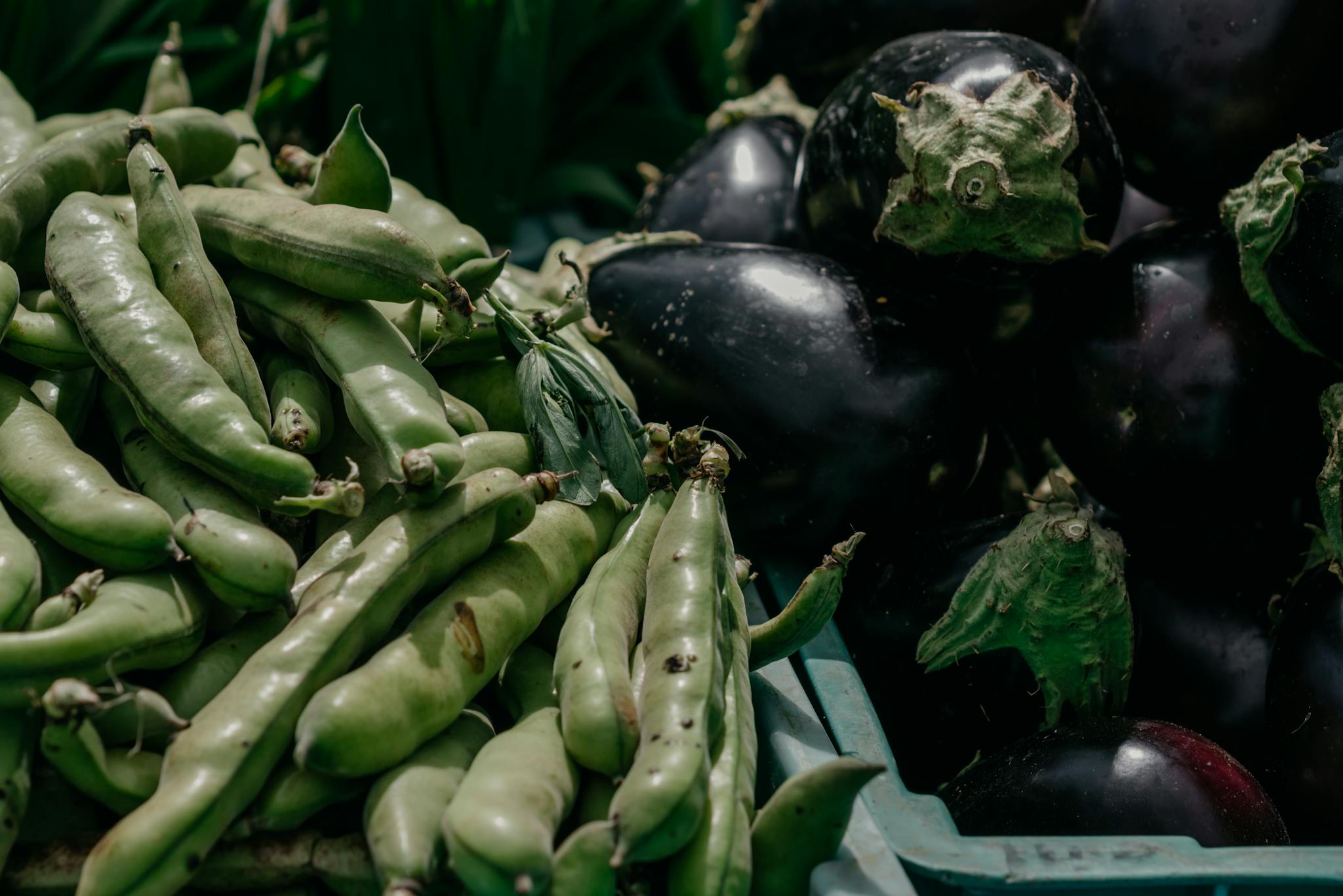 Close-up of eggplants and snap peas at a farmer's market showcasing fresh organic produce.